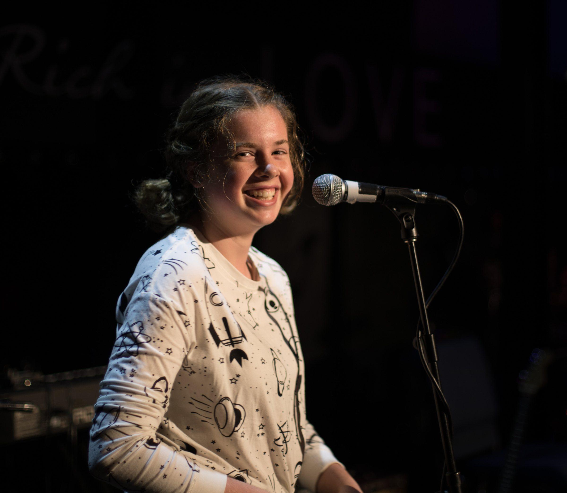 A smiling young voice student holding a microphone